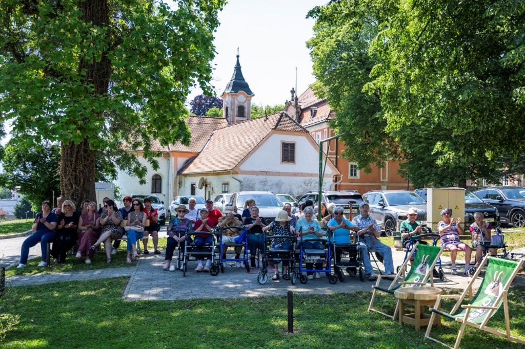 Skupni trenutki veselja: stanovalci, gostje in zaposleni uživajo v živahnem dogajanju pod prijetno senco dreves.